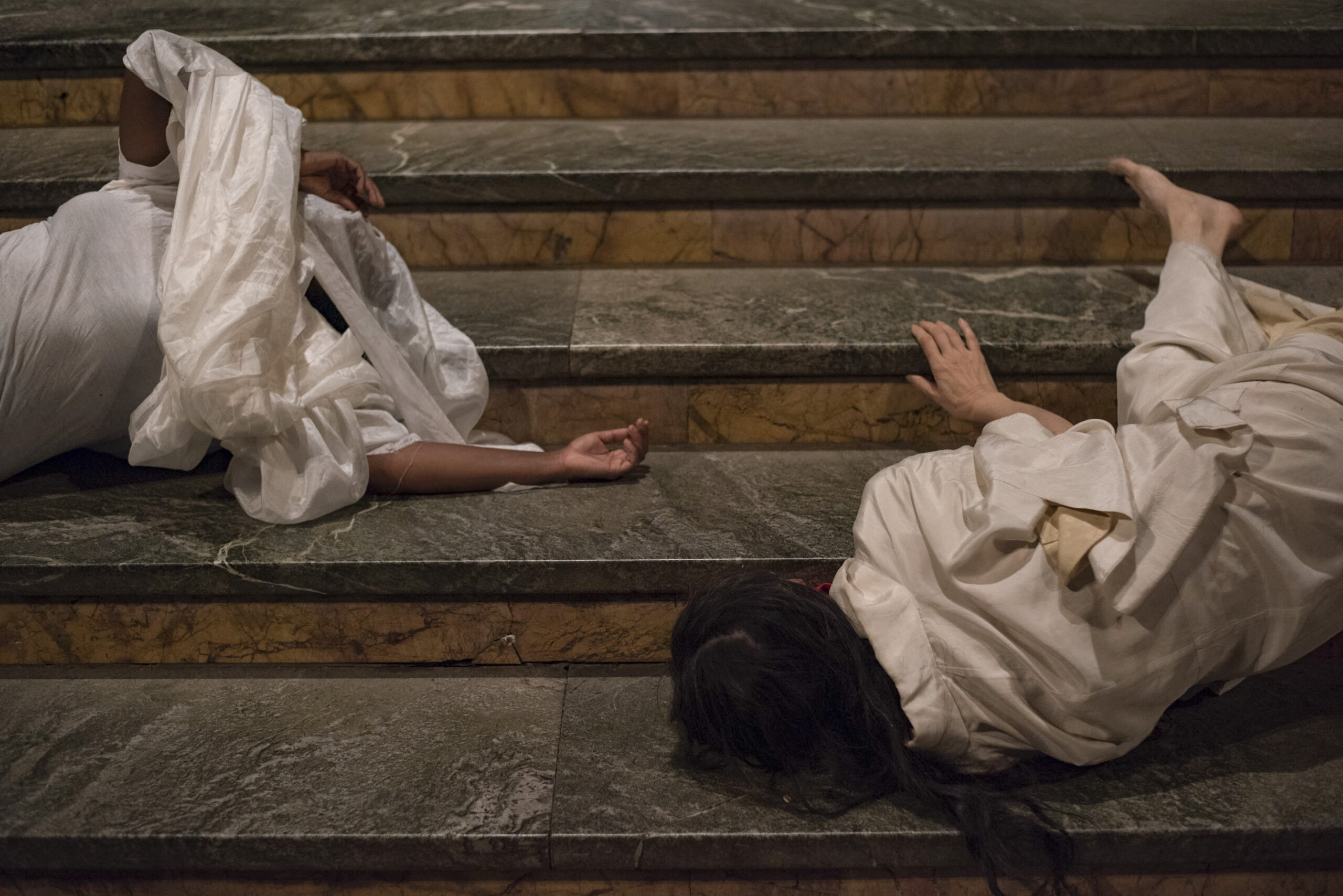 Photo of two women draped in white fabric rolling down the stairs of Cathedral of St. John the Divine.