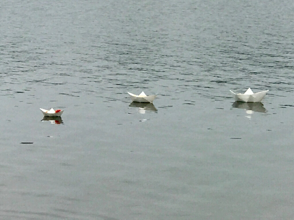 Three white paper boats float on rippling water.