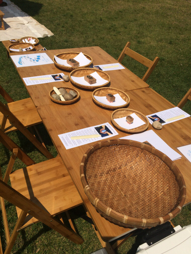 Papers and wicker baskets are laid out on a wooden table, surrounded by wooden chairs.
