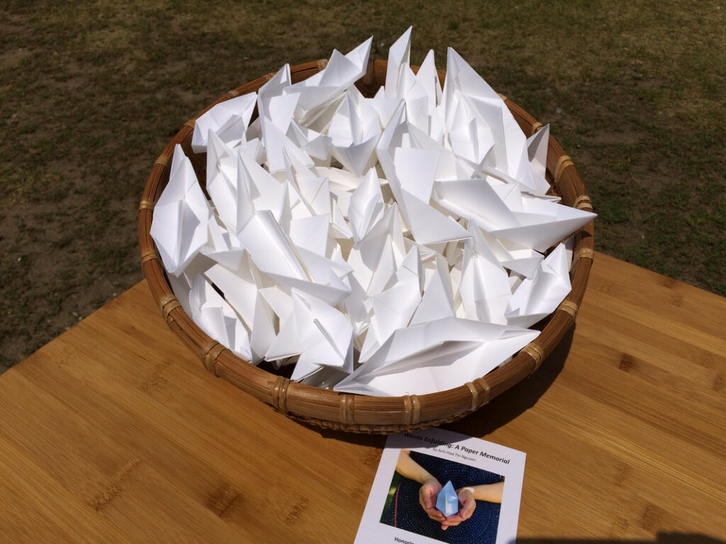 A wicker basket full of many white paper boats sits on a wooden table.