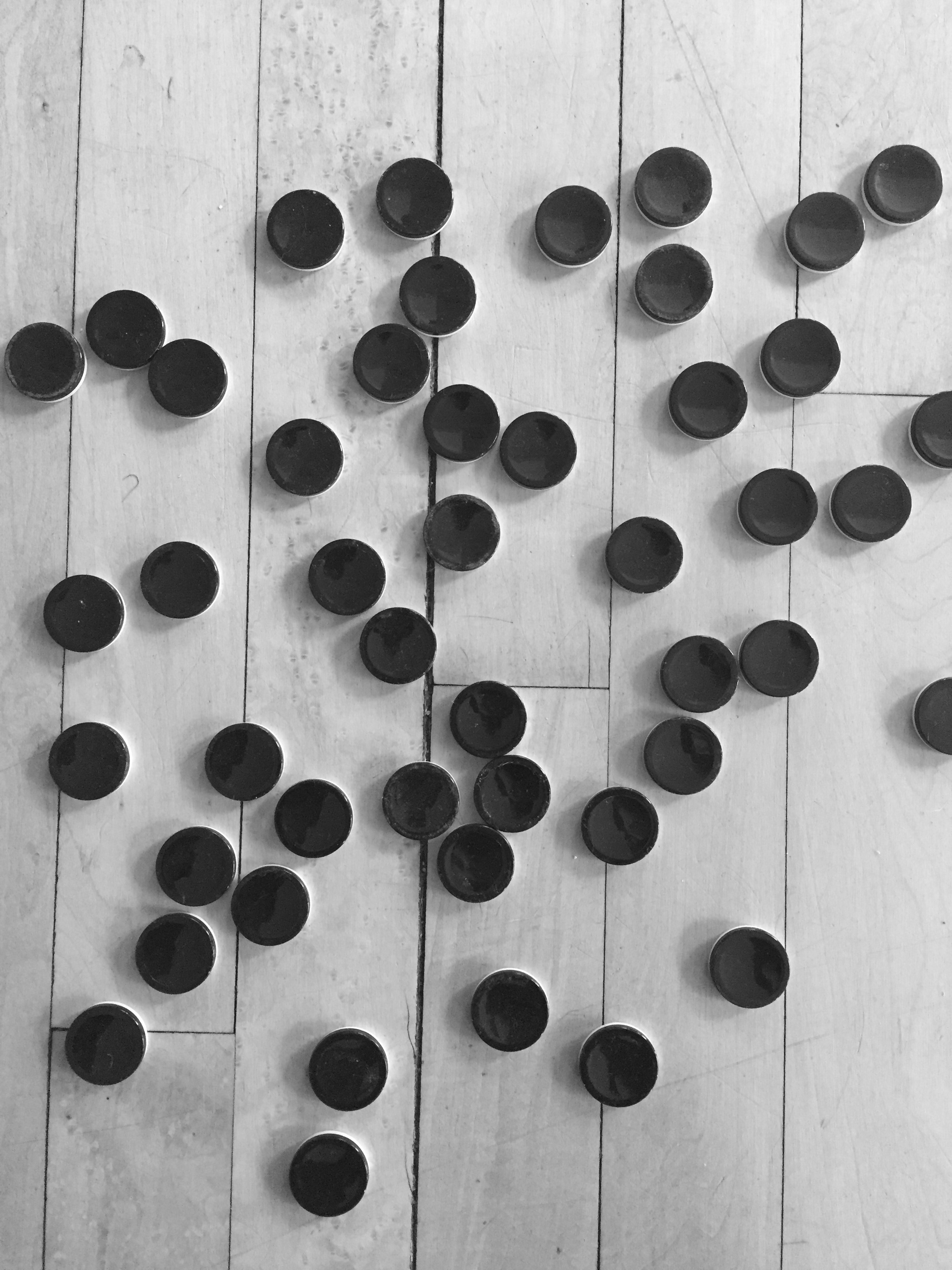 Black and white photo of black bottle caps on a wooden floor
