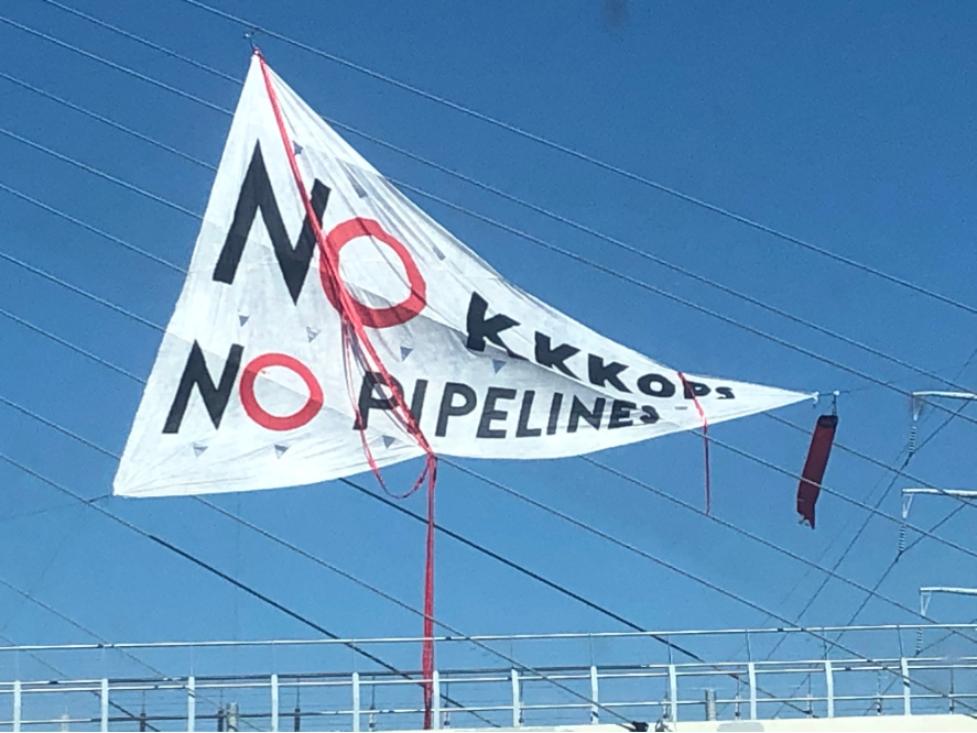 Triangular banner against blue sky reads: NO KKKOPS / NO PIPELINES.