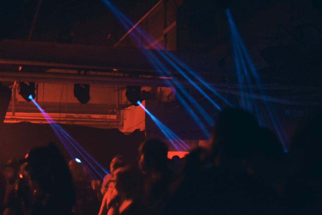 Beams of blue light shine into a dark dance floor, with a wall lit in red.