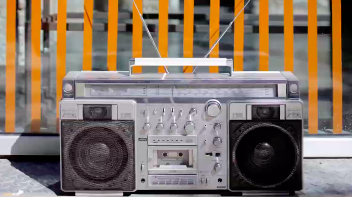 Silver boom box in front of background with vertical orange stripes.