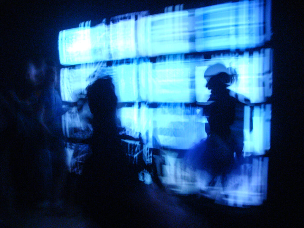 Blue light from a bank of TV screens, with silhouettes of two people.