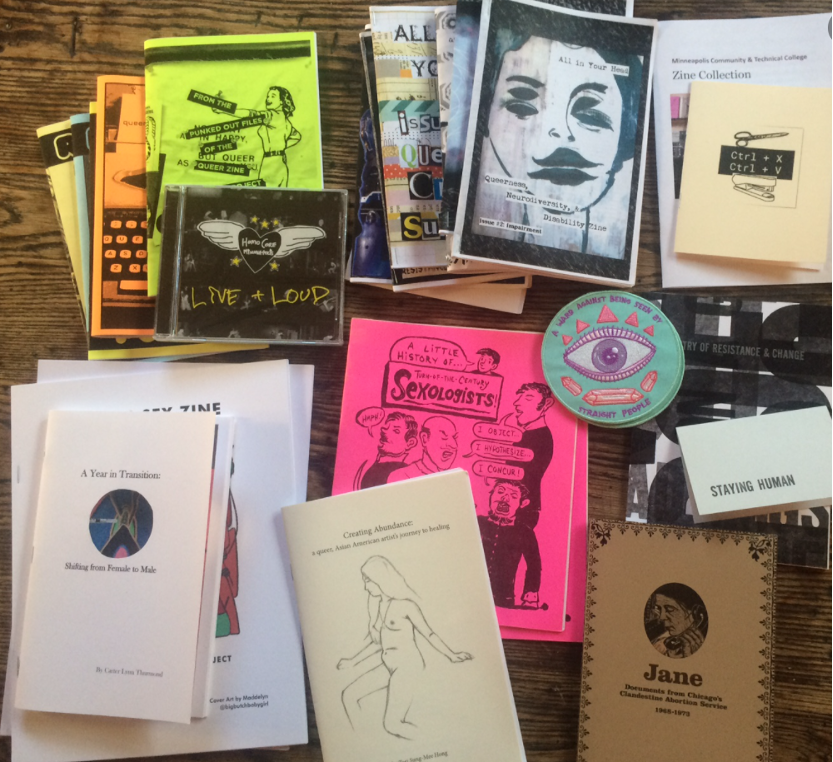 Many zines in neon colors spread out on a surface, with a prominent drawing of a face.