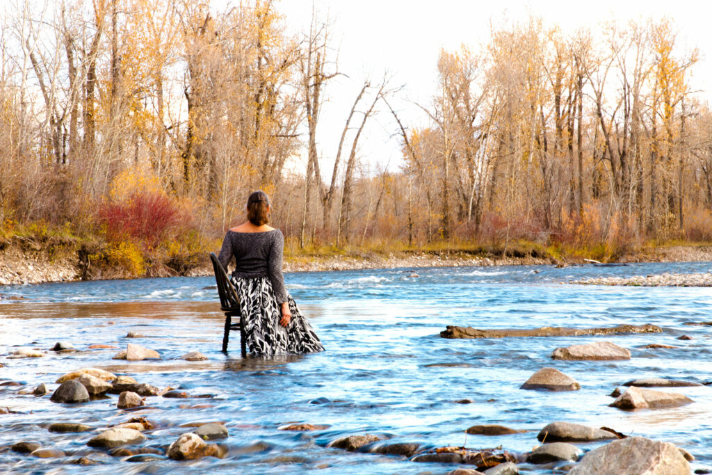 Person wearing a long skirt sits in a chair in the middle of a rocky creek.