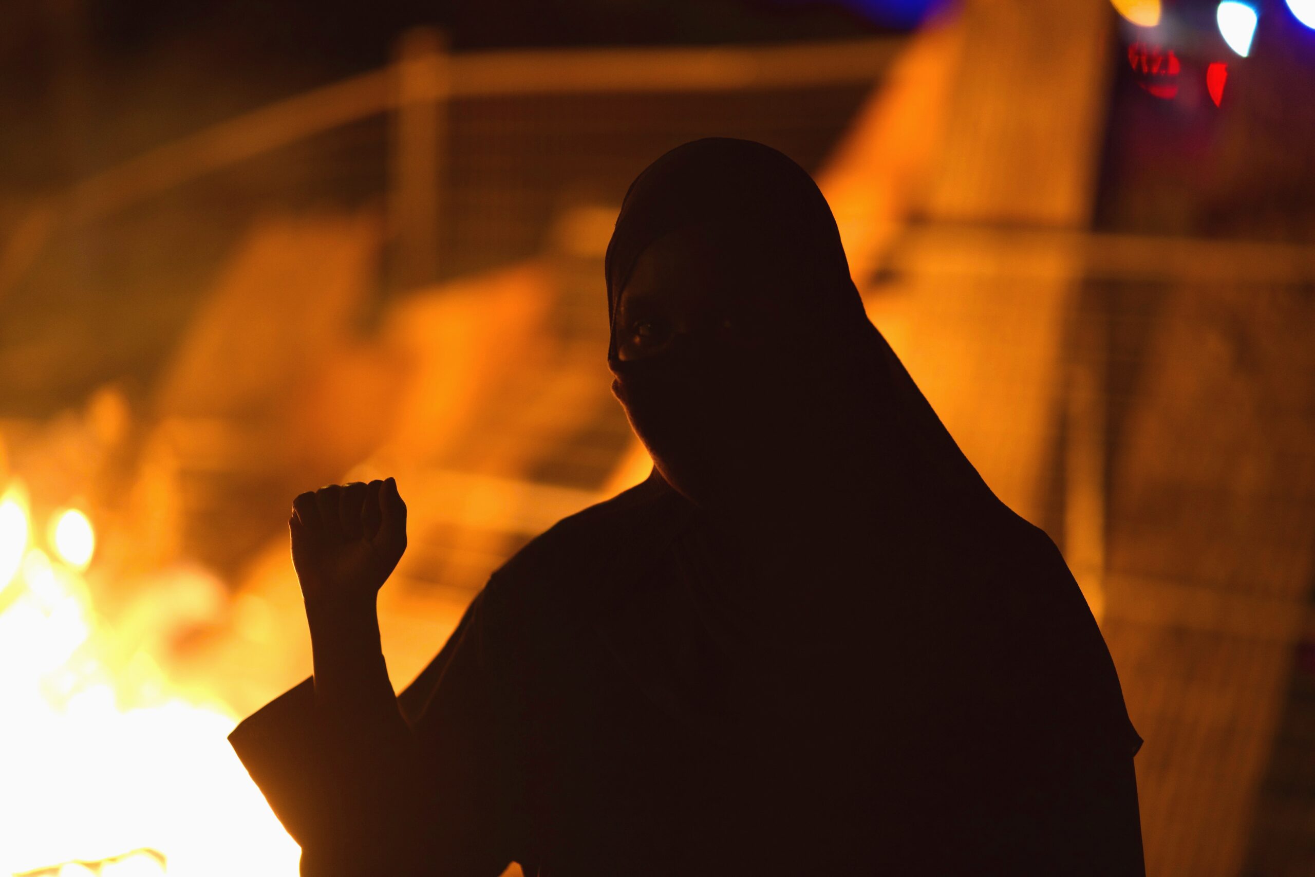 Silhouette of a person with fist raised, with fire glowing in background.