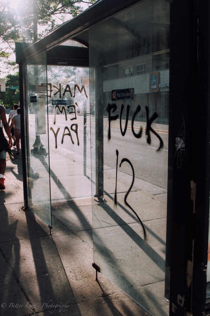 Light shines through glass bus shelter, with tag reading "FUCK 12."