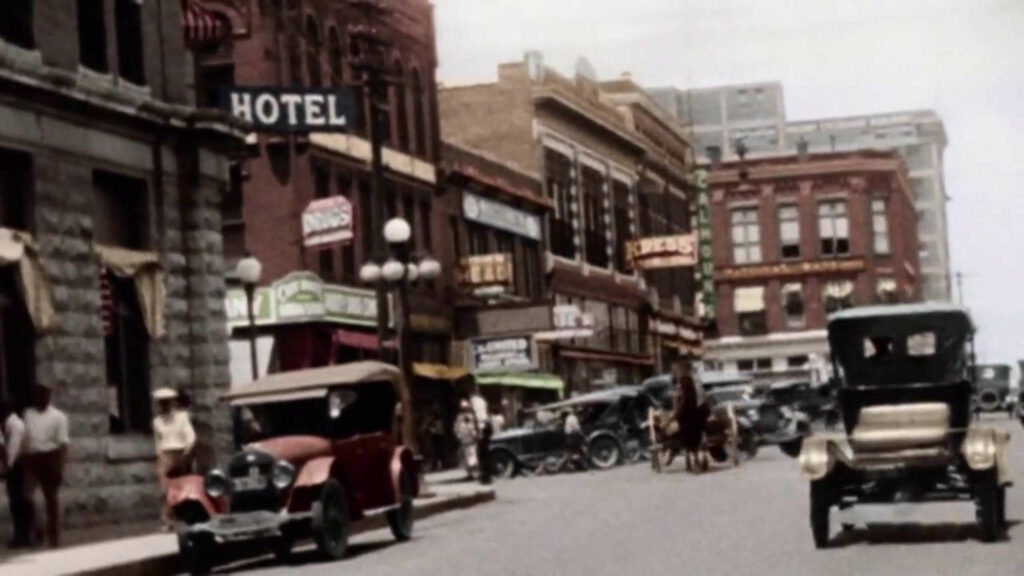 Vintage photograph of busy street scene with cars and brick buildings.