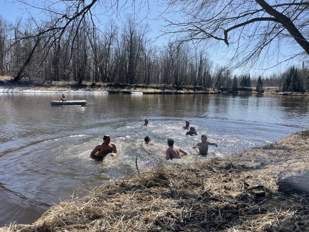 Group of people swims in a river, with dry grass and leafless trees.