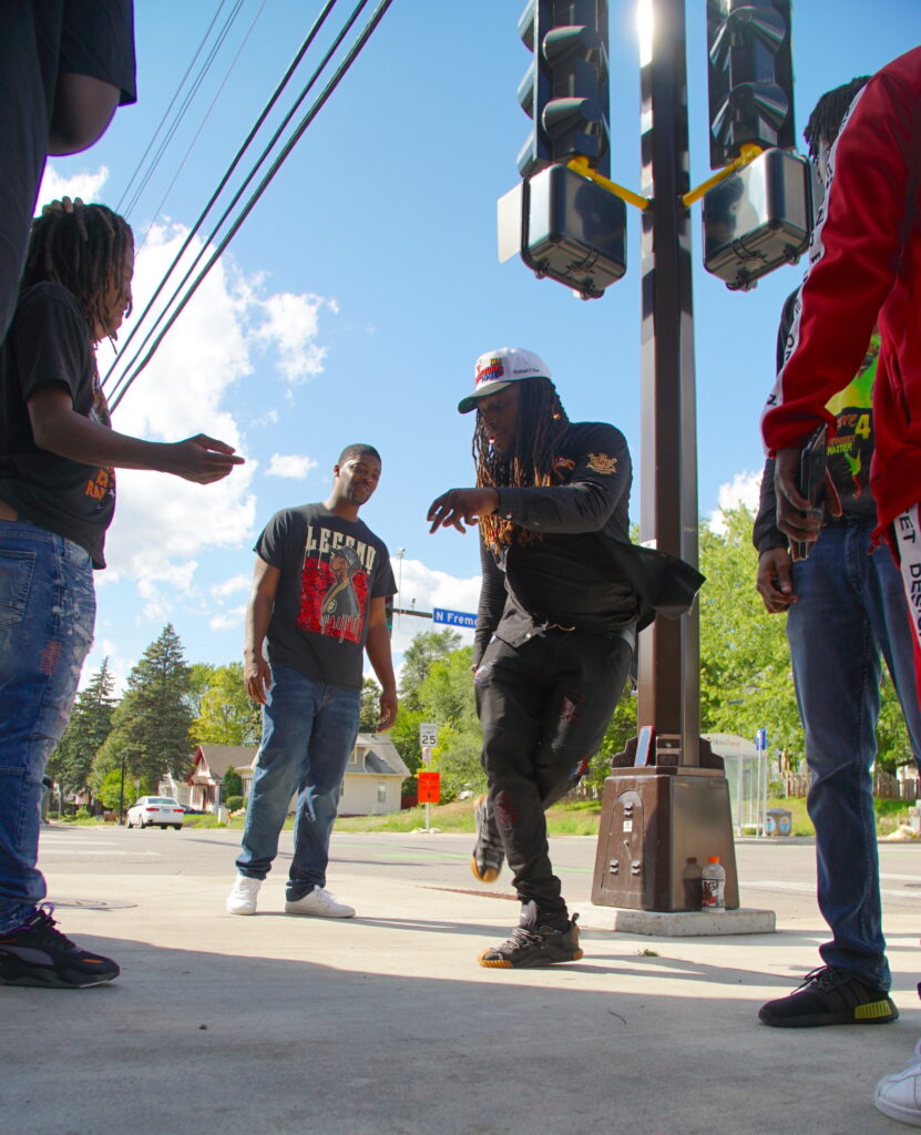 Group of people gathered around dancer on street corner.