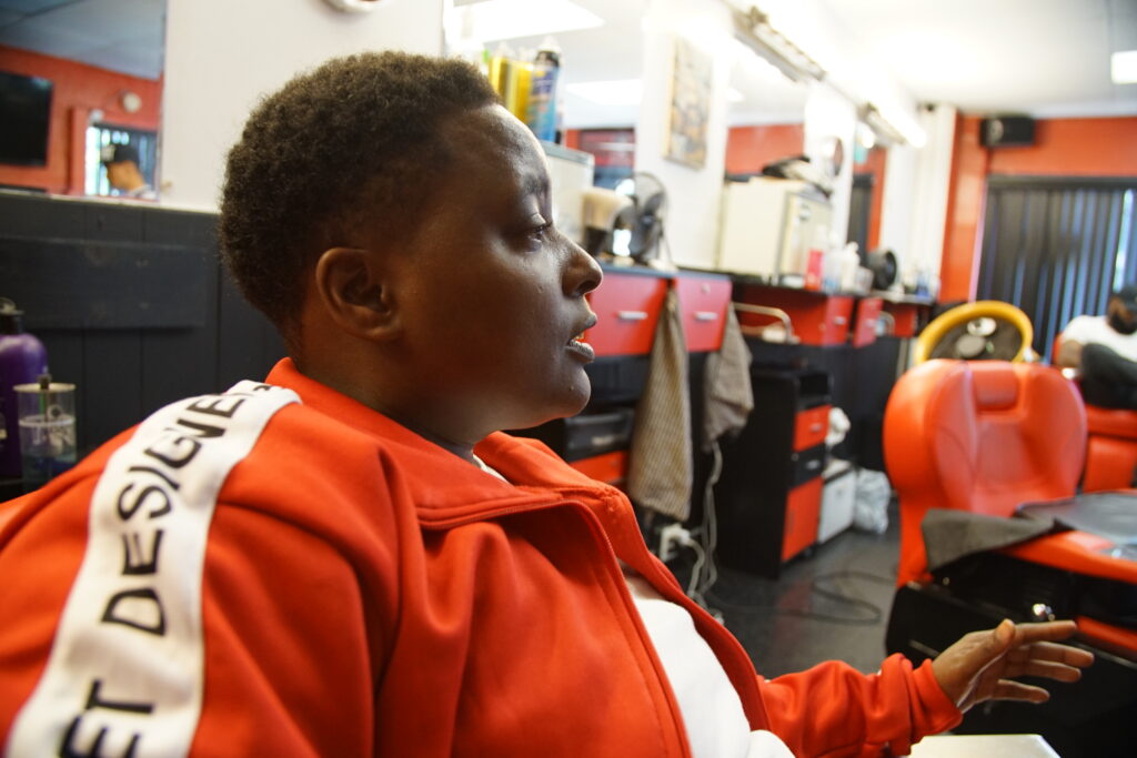 Person with dark skin and red sweatshirt in profile inside barber shop.