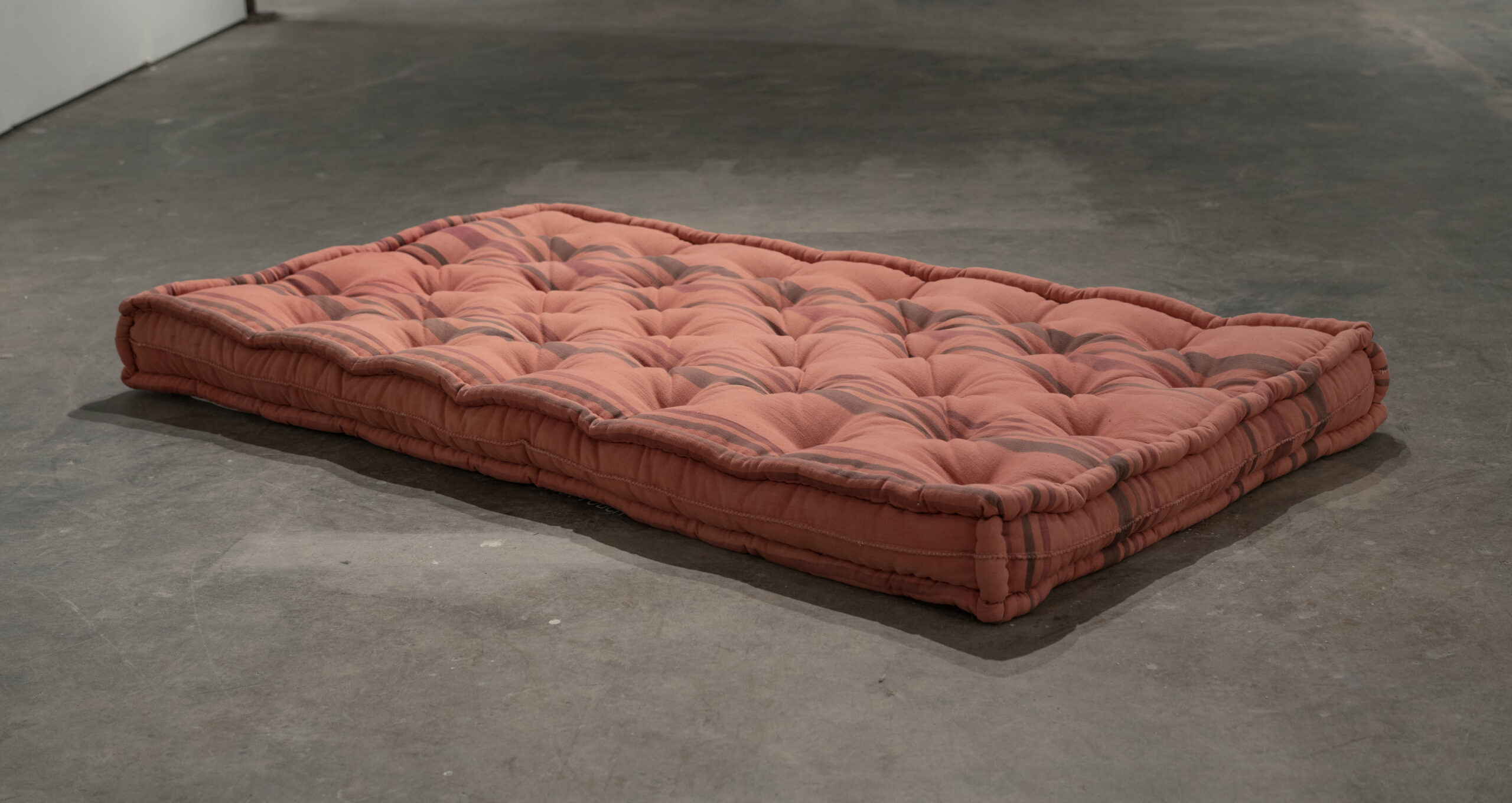 Rust-colored, tufted mattress on gray floor.