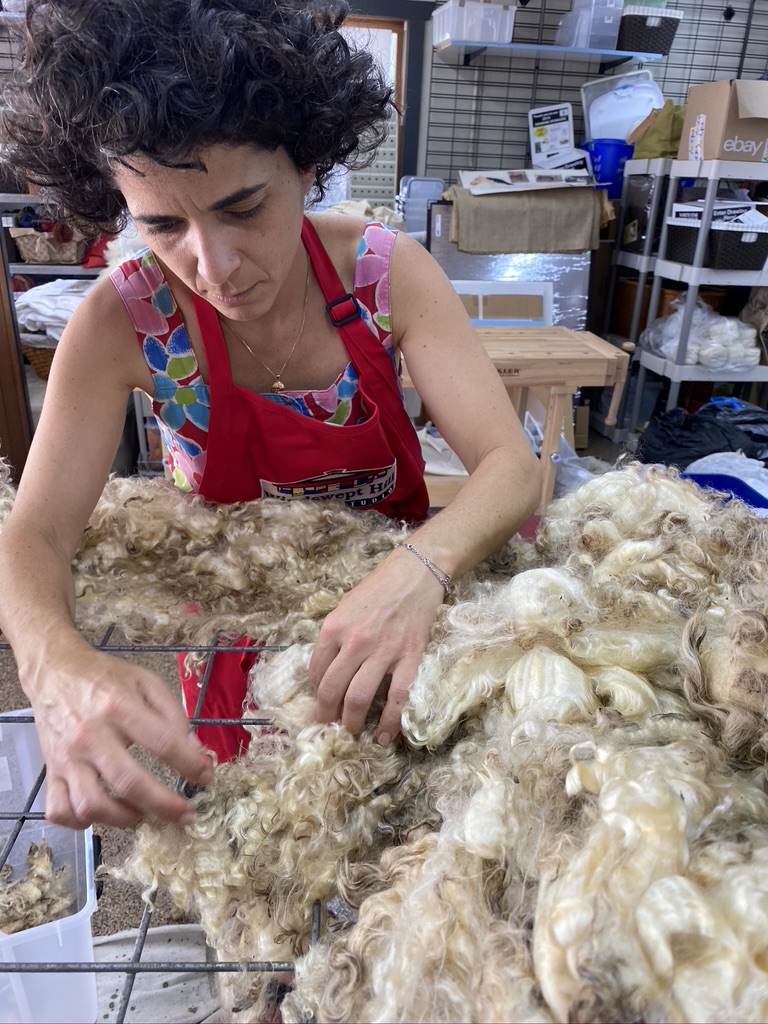 Person wearing red apron digs their hands into piles of wool.