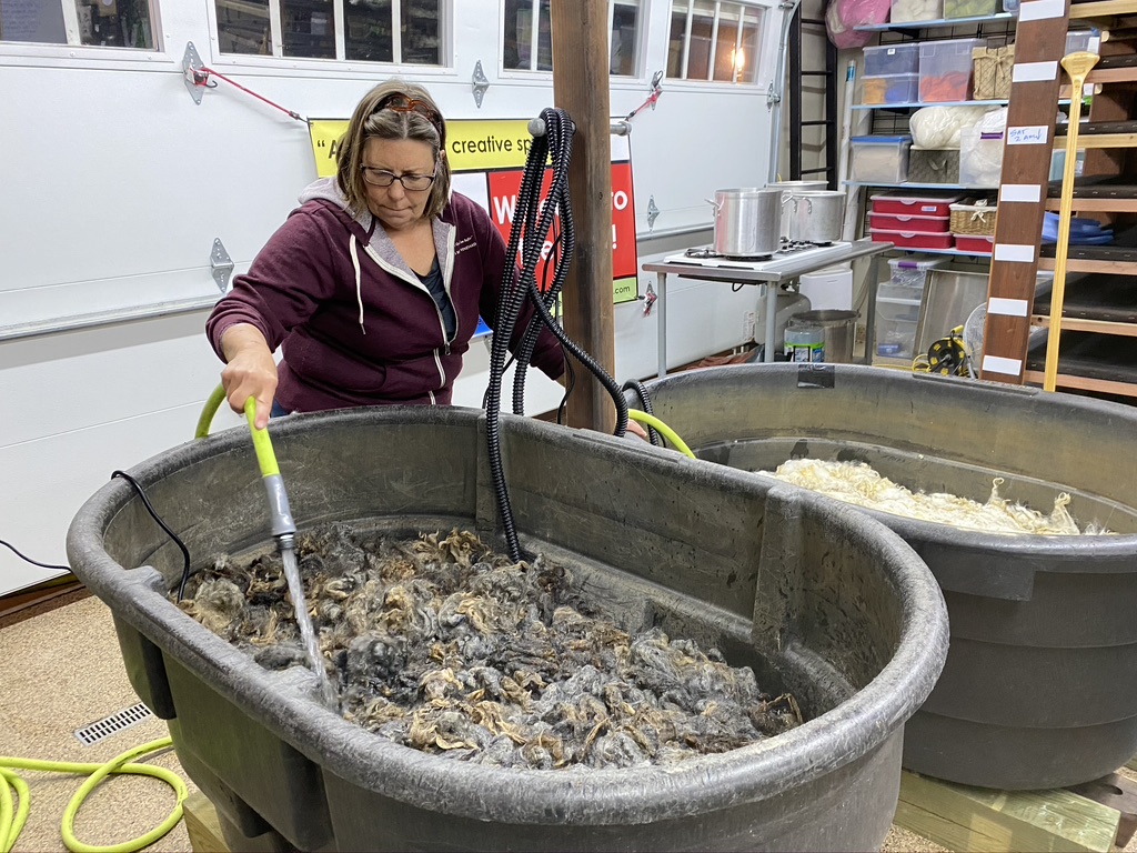 Person with medium brown hair stirs a large basin full of wool and water.