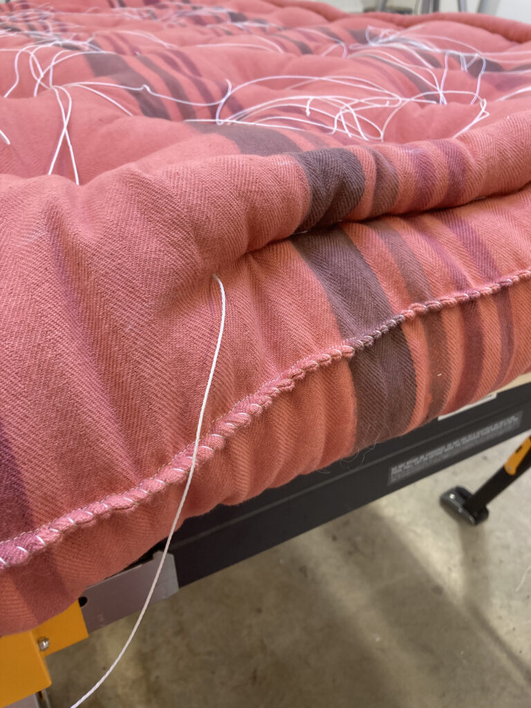 Sewing the edge of red fabric mattress with white thread.