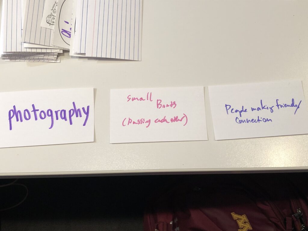 Three index cards laid out on a table, reading left to right: photography / small boats (passing each other) / people making friends/connection