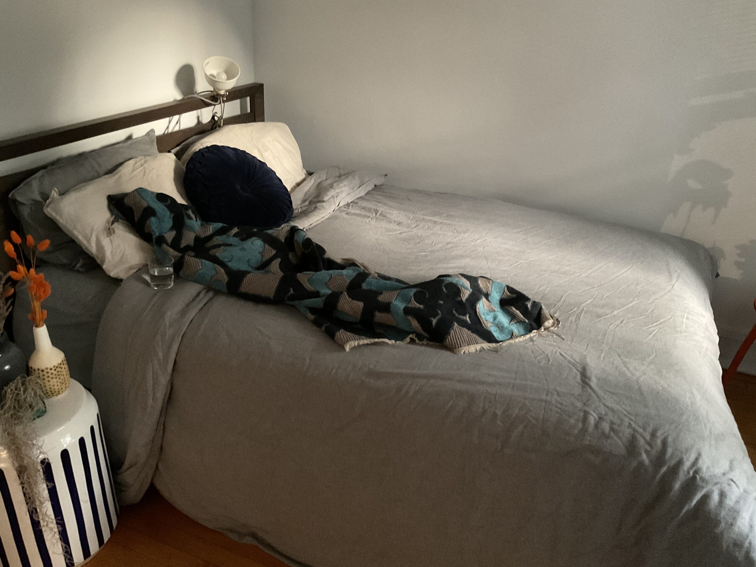 Blue patterned blanket lies on bed with gray bedspread with glass of water beside it.