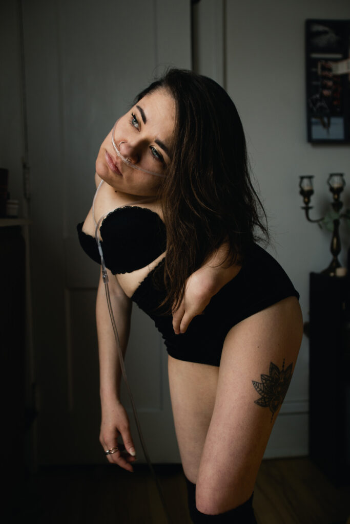 A photo portrait of Trista, wearing a black bra and underwear. She is looking to the left of the frame and her long brown hair is resting over her shoulder.