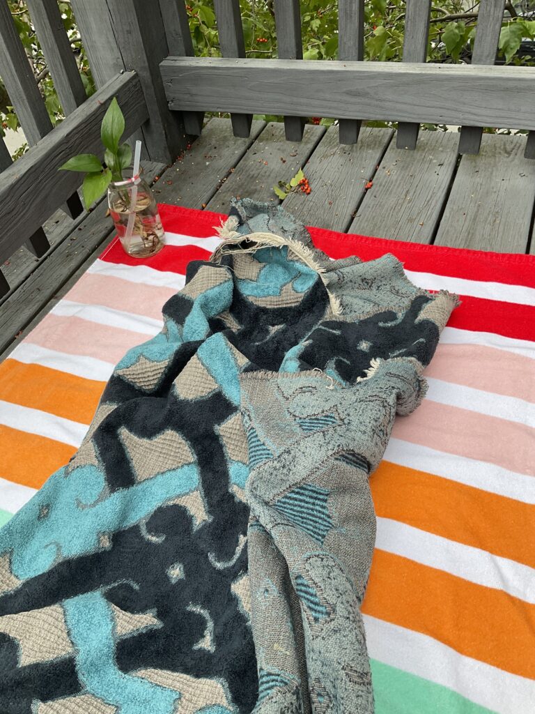 Blue patterned blanket lies on brightly striped towel on a wooden deck.