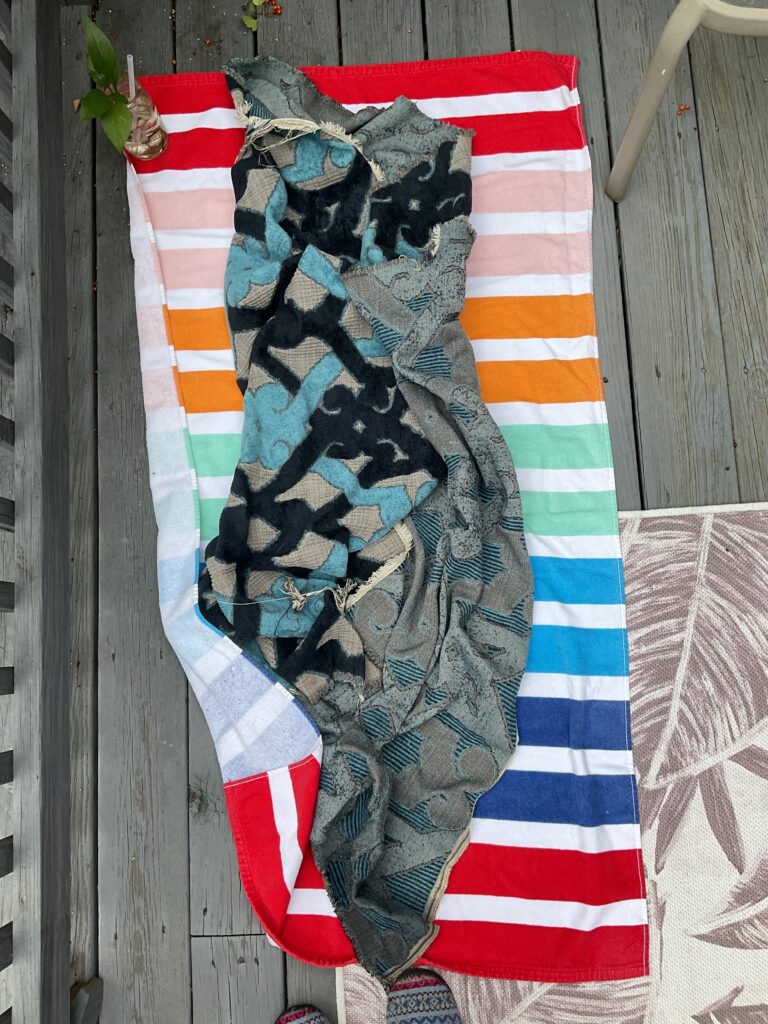 Blue patterned blanket lies on brightly striped towel on a wooden deck, viewed from above.