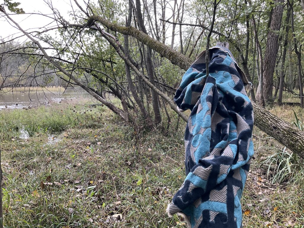 Blue patterned blanket folds over fallen tree branch, with water in background.