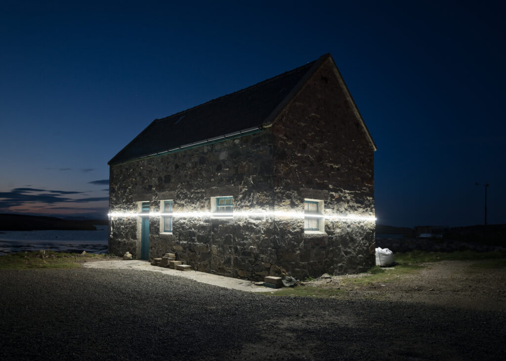 Stone house at night, with band of white light running around its circumference.