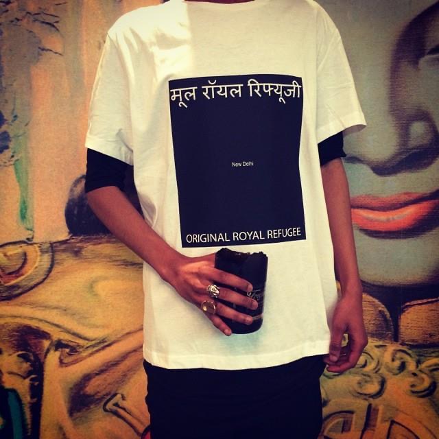 Person wears white t-shirt with black box reading "New Delhi / Original Royal Refugee."