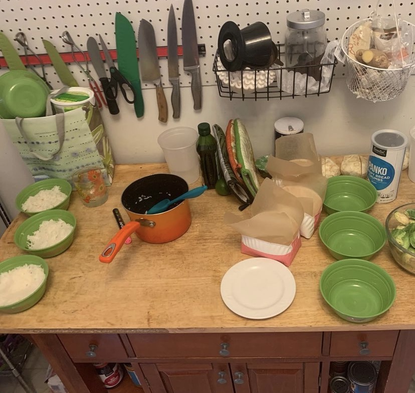 Kitchen counter with lots of equipment, many bowls of food, and knives on wall.