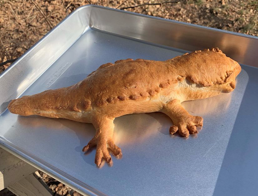 Bread in the shape of a gecko rests on silver pan.