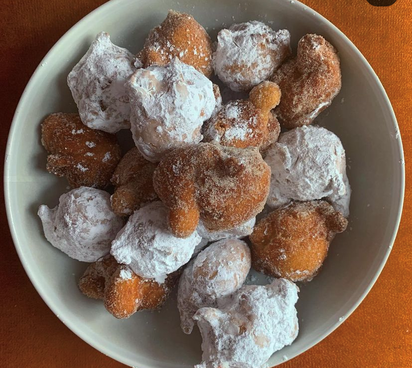 Bowl of handmade doughnuts, some with powdered sugar.