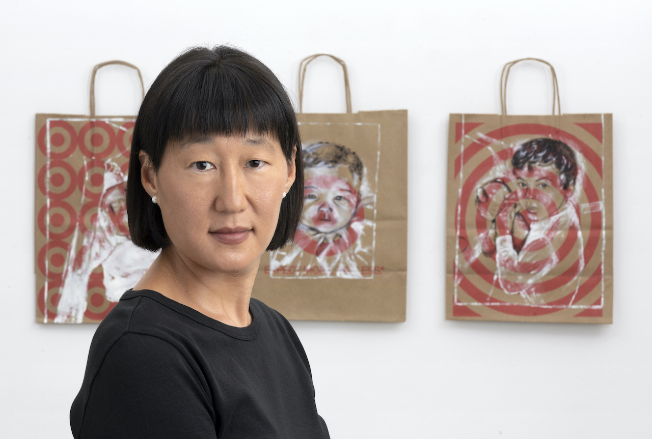 Person with a bob haircut standing in front of three portraits of infants painted on brown shopping bags with red Target logos.