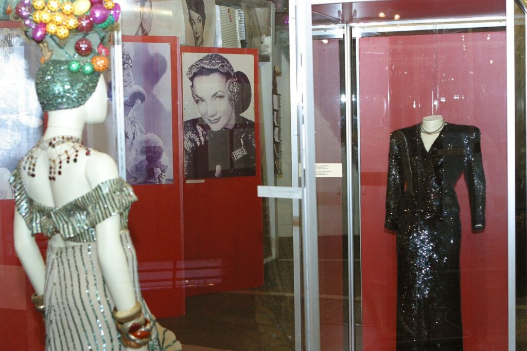 Mannequins with sparkly dresses and headdress, next to photo display of person wearing headdress and smiling.