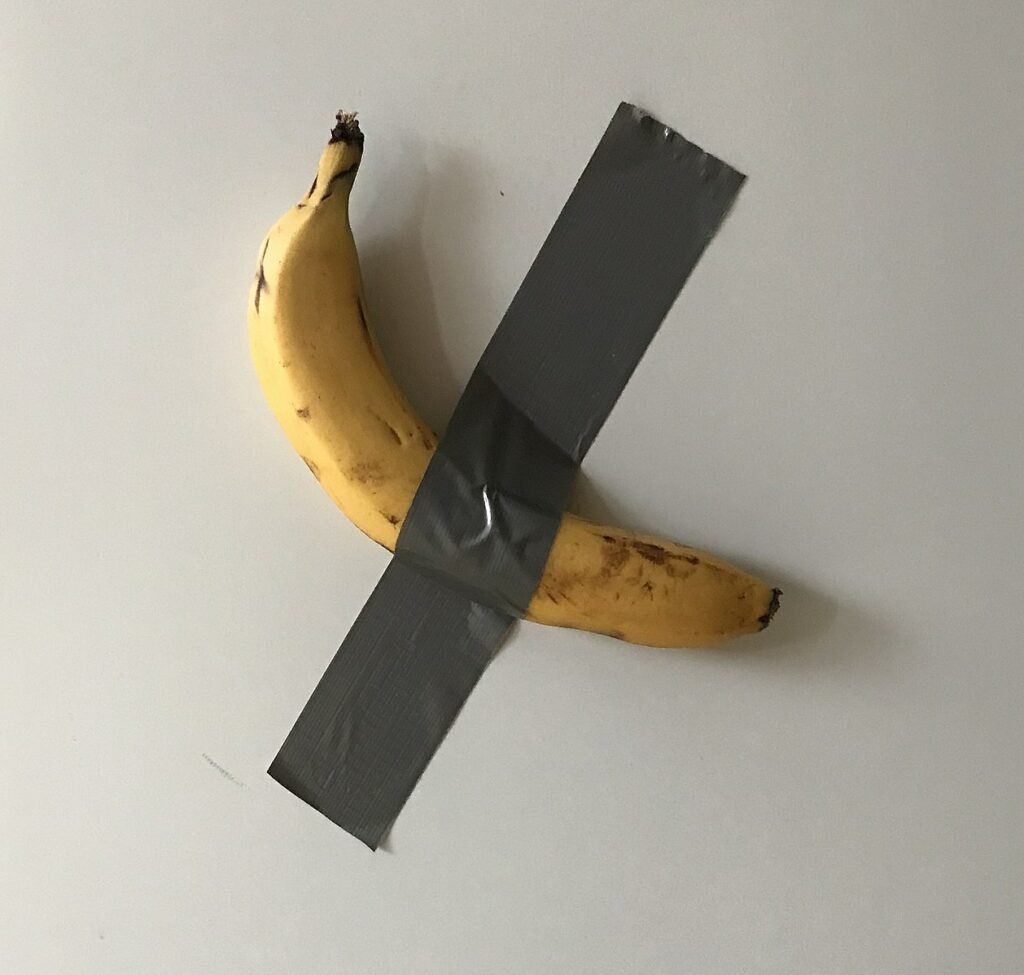 Strip of silver duct tape holds a banana to a white surface.