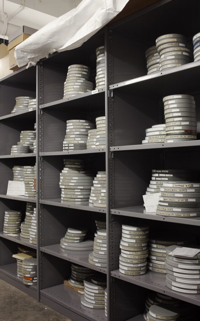 Gray shelving with many stacked rolls of film with white labels.