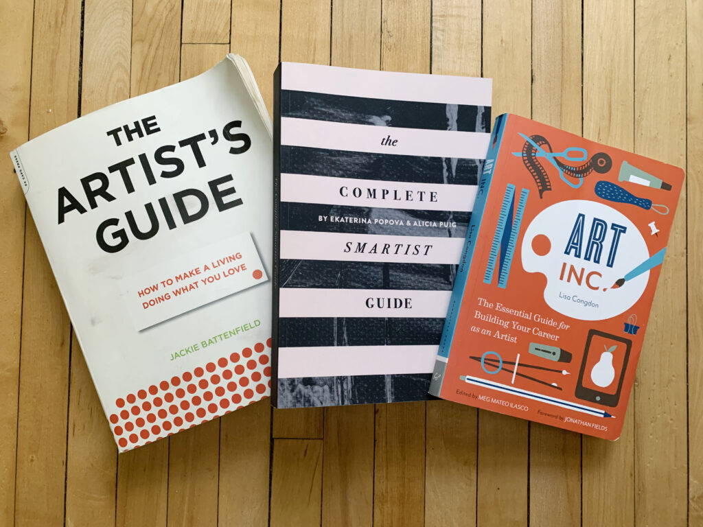 Three books laid out on wooden floor: The Artist's Guide, The Complete Smartist Guide, and Art, Inc.