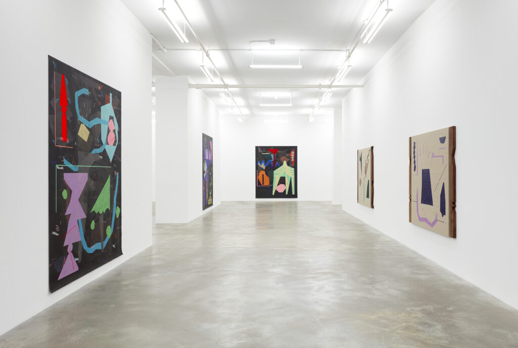Large white-walled gallery with many large paintings hung on walls, with multicolored abstract shapes on black background.