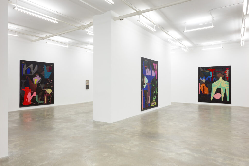 Large white-walled gallery with three large paintings hung on walls, with multicolored abstract shapes on black background.