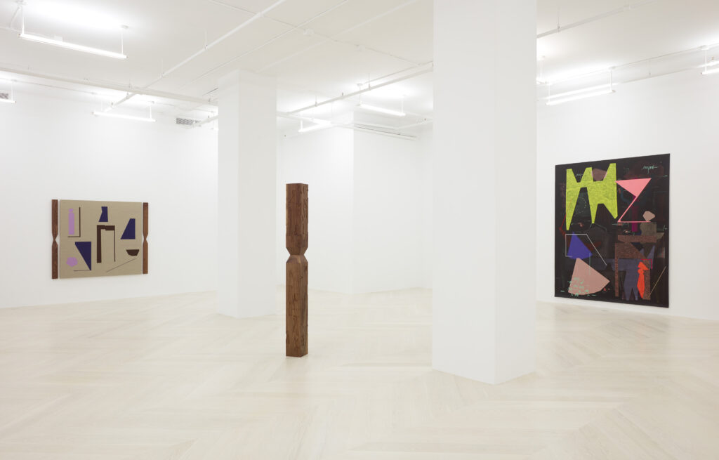 Large gallery with white columns, two abstract paintings hung on walls, and obelisk sculpture in center.