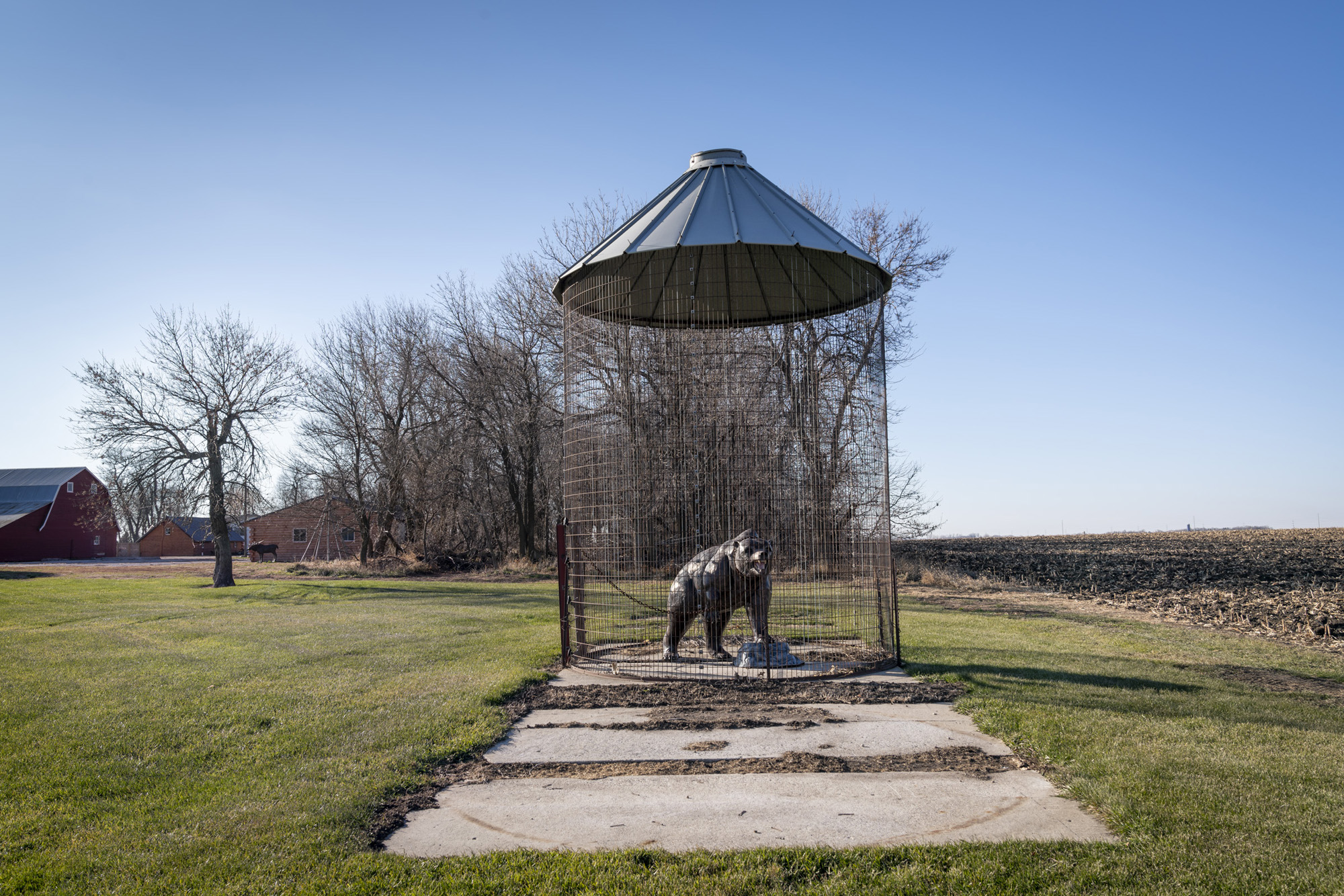 Photograph of farmland with a sculpture of a bear inside of an old corn crib