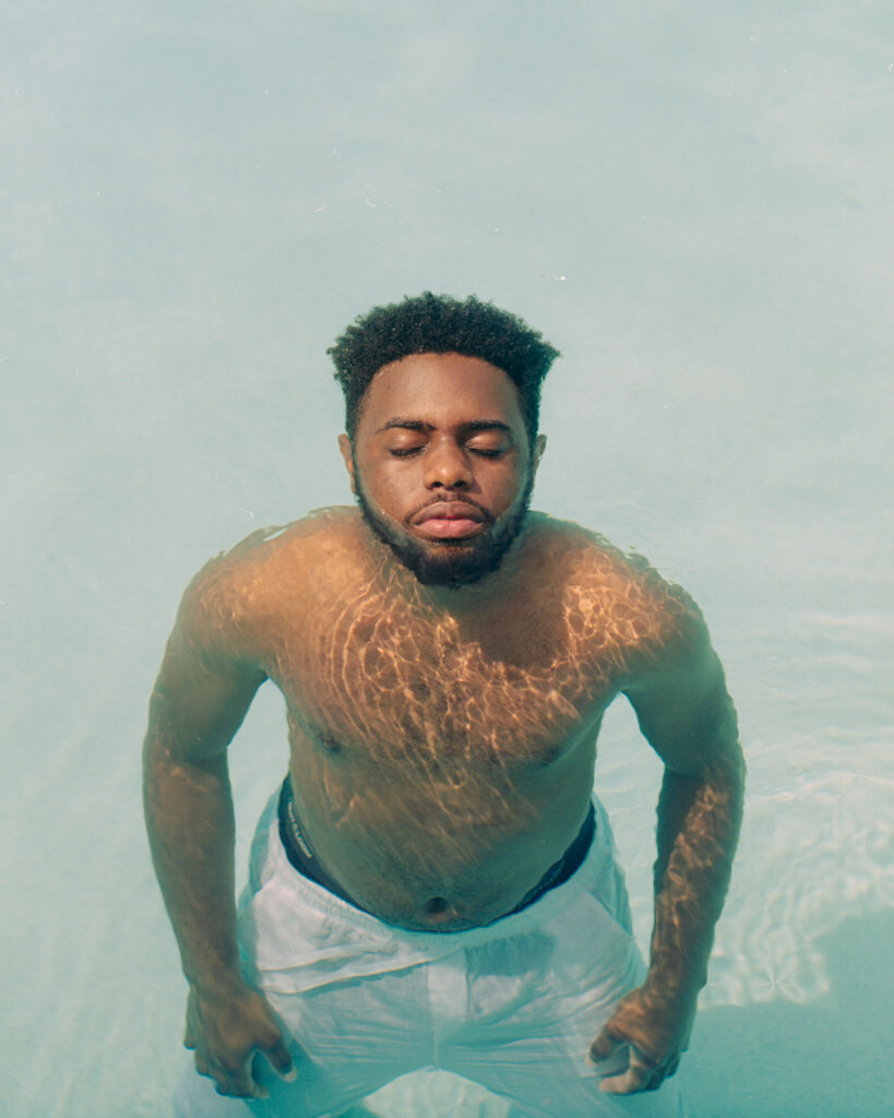 Photo of a man with dark skin with all but his face submerged in clear water.