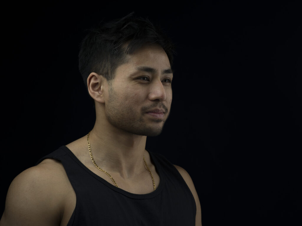 Angled portrait of a person with a slight smile staring away against a black background.