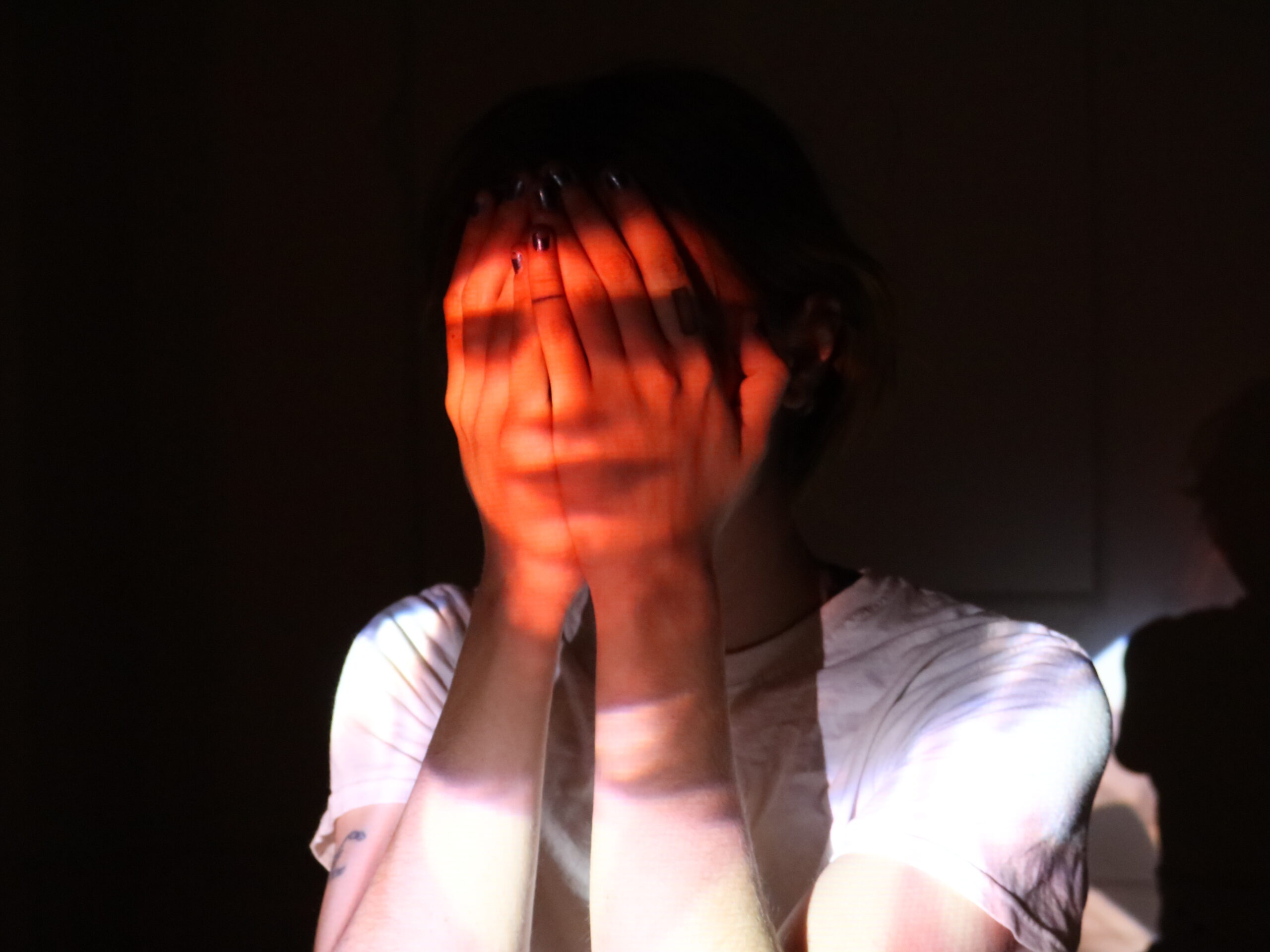 Person with light skin covers their face with their hands, while image of face is projected onto their hands.