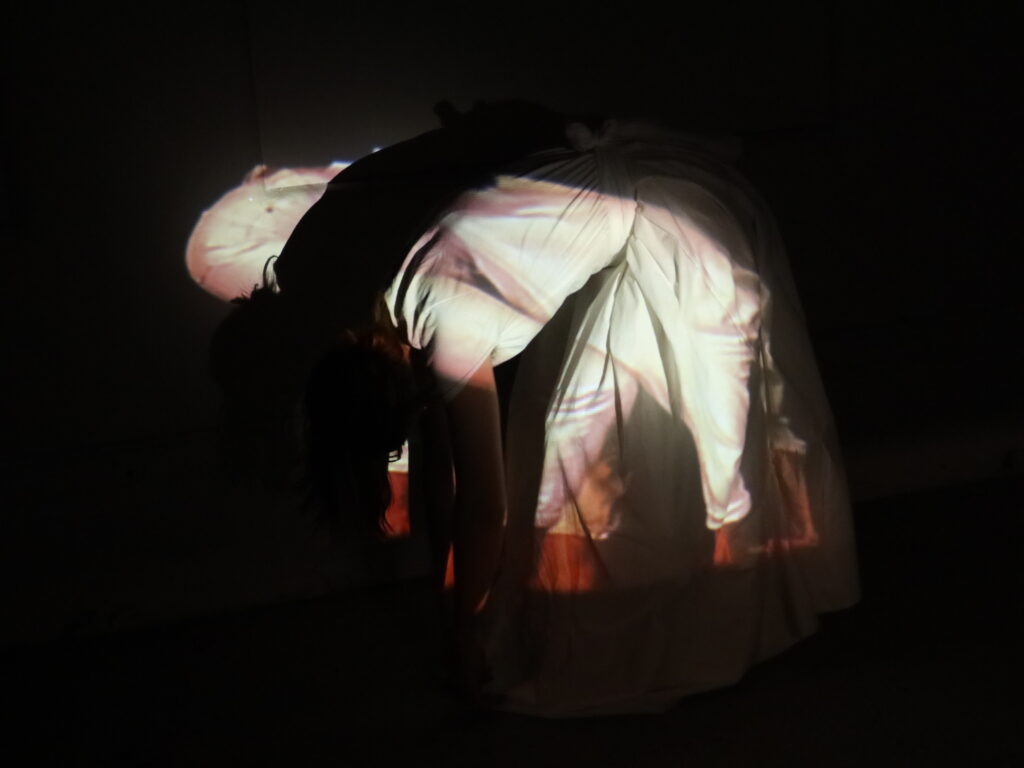 Person wearing white bends their torso to the side in pool of projected light.