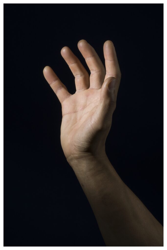 Photograph of a light skinned hand open to light angled toward it against a black background.