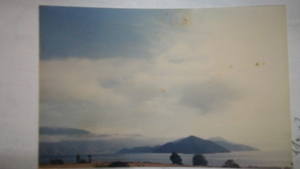 Faded photograph of lake with islands, white clouds, and blue sky above.