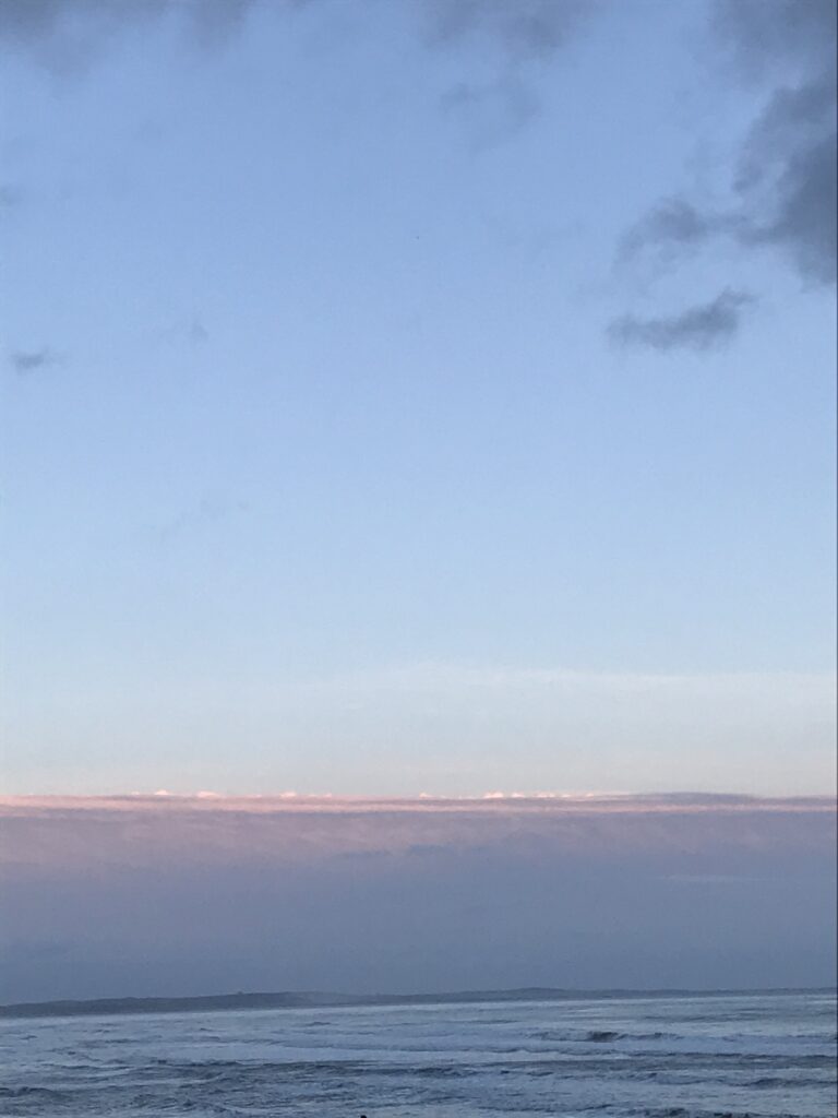 Blue sky with line of pink clouds over calm blue sea.