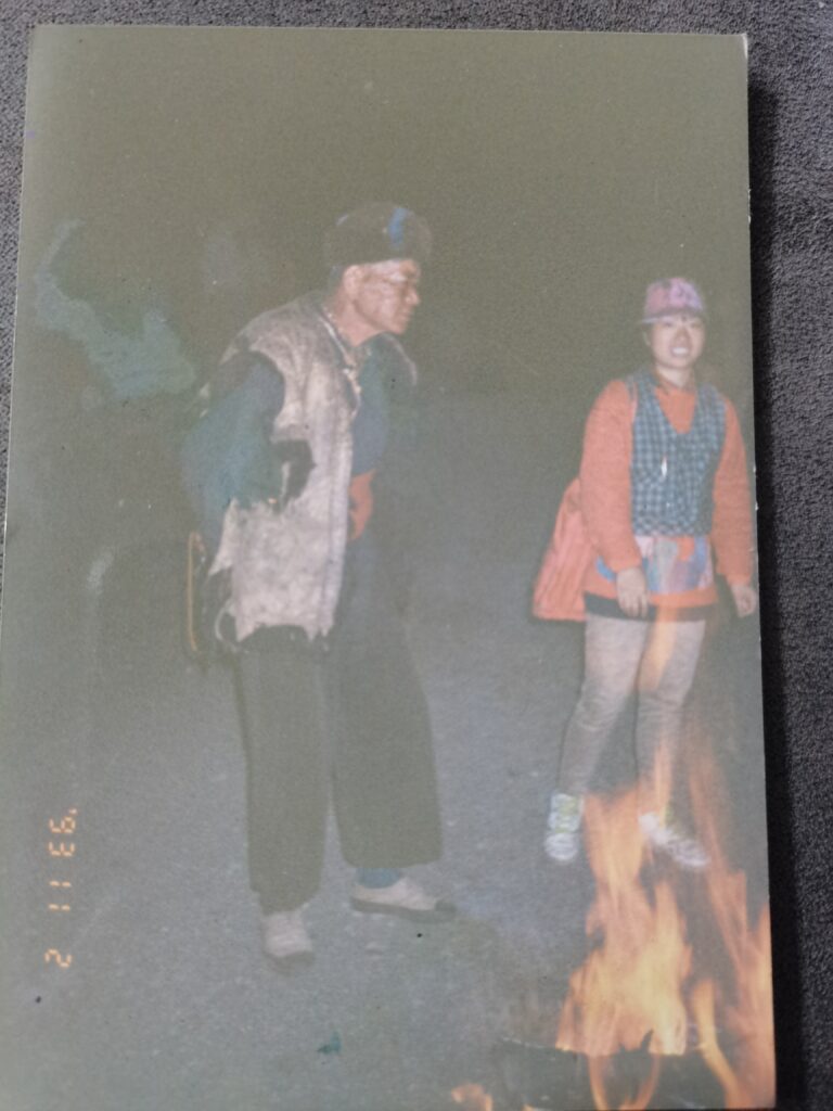 Faded photograph of two people standing in front of fire.