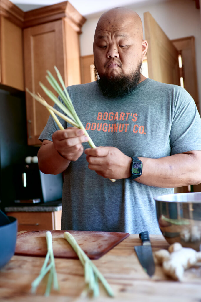 Yia Vang wears gray Bogart's Doughnut Co. t-shirt and holds up bunch of lemongrass.